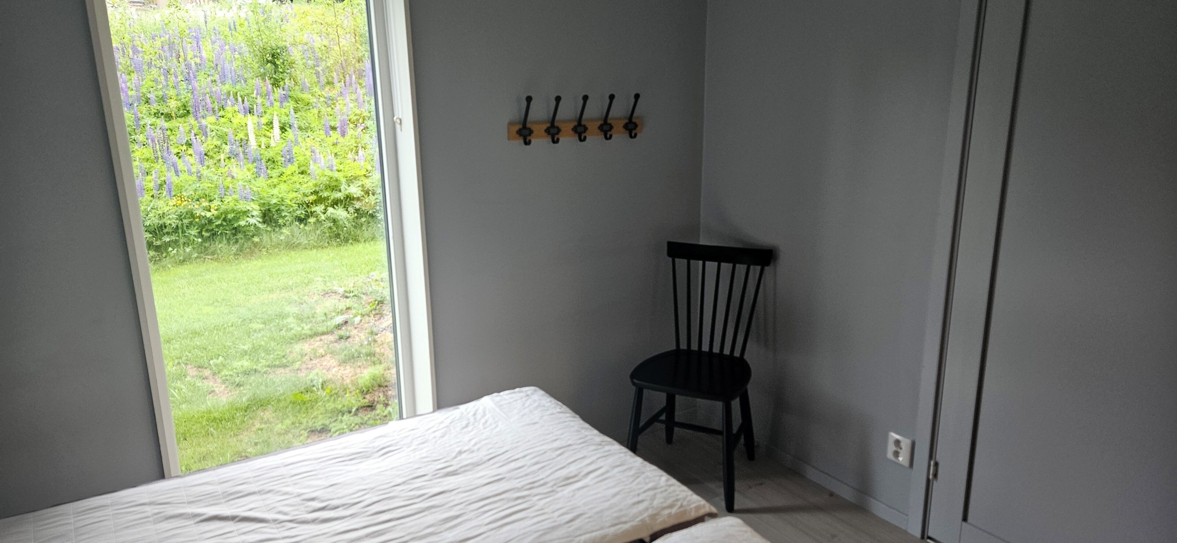 A bedroom with a bed, a chair, a window, and a coat rack.