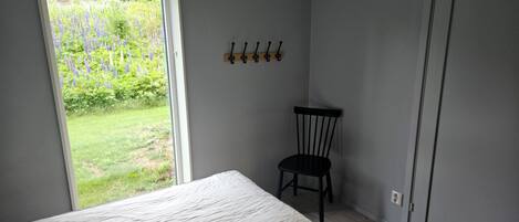 A bedroom with a bed, a chair, a window, and a coat rack.