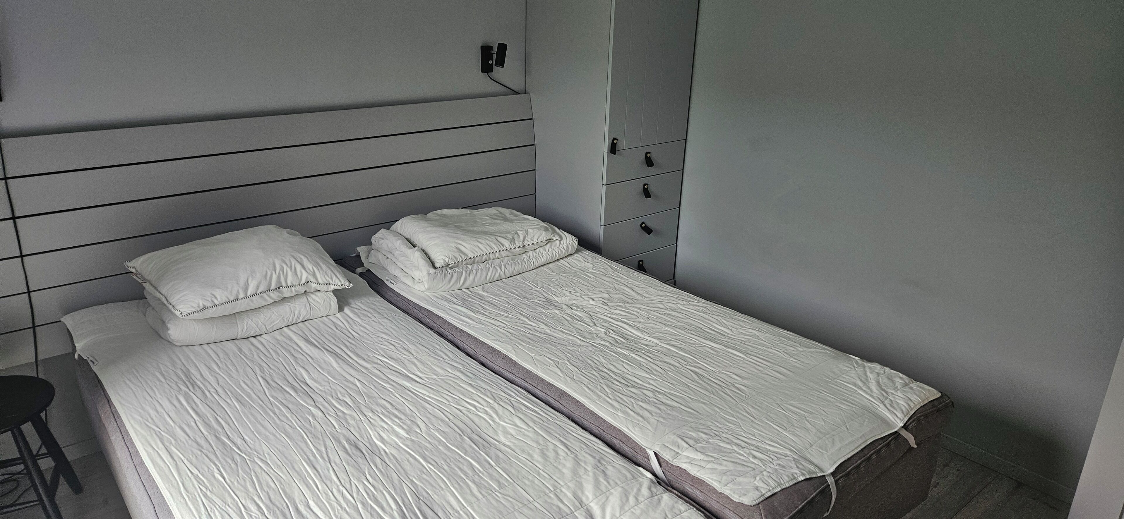 Une petite chambre avec un lit simple, une tête de lit grise et une armoire dotée de plusieurs tiroirs.