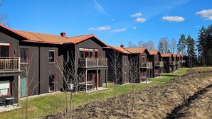 A row of modern, dark-colored cabins with red accents, featuring balconies and large windows. - Skidvägen 4a - Lodge (Jarvso)