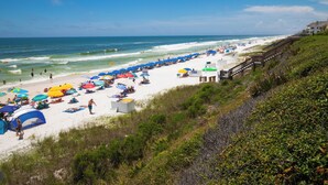 A beach with white sand, blue umbrellas, and a wooden walkway.