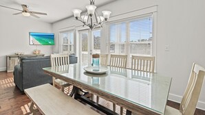 A dining area with a glass table, wooden chairs, a chandelier, and a ceiling fan. - Golf Cart, Great Location, Close to Beach Access (Santa Rosa Beach)