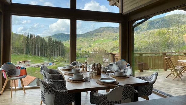 A dining area with a table set for four, large windows offering a view of a mountainous landscape. - Chalet Alpage 10 persons (Bussang)