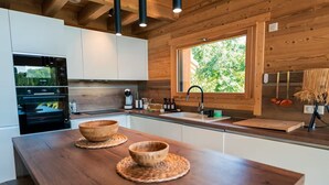 A modern kitchen with wooden cabinets, a Bosch oven, a large window, and a wooden island with bowls. - Chalet Alpage 10 persons (Bussang)