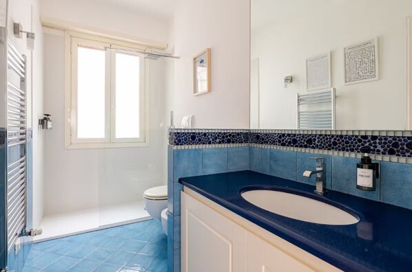 A bathroom with a blue tiled floor, a white sink, and a shower area.