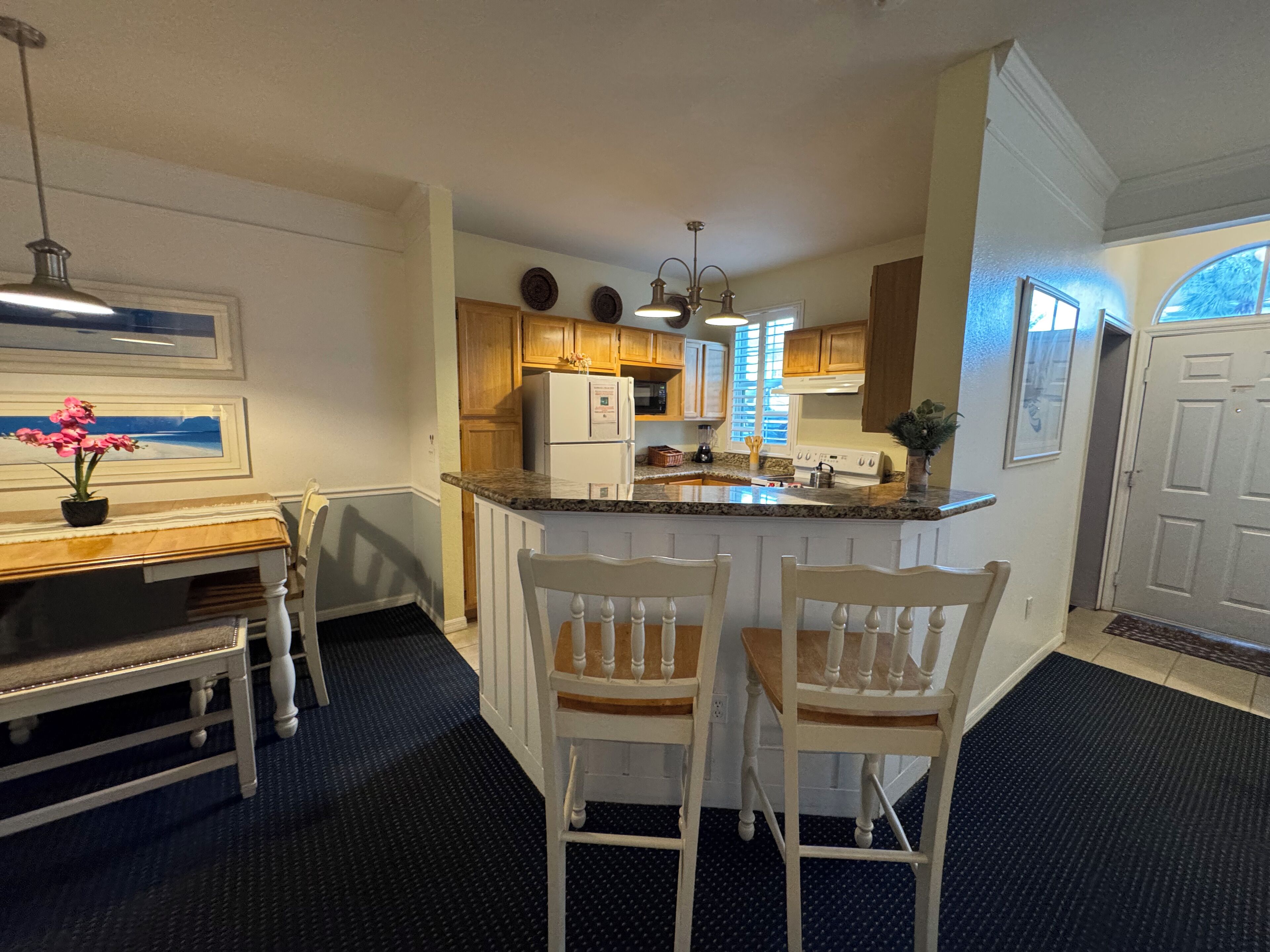Una cocina con una isla central, armarios de madera, un refrigerador y un comedor con mesa y sillas.