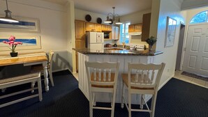 A kitchen with a central island, wooden cabinets, a refrigerator, and a dining area with a table and chairs. - ★Full Equipped Villa 8 guests 2Br/2Bth Pool and Free Shuttle to Disney Parks★ (Kissimmee)