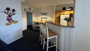 A hotel room with a Mickey Mouse mural, a dining area with a table and chairs, a kitchen with wooden cabinets, and a blue door. - ★Full Equipped Villa 8 guests 2Br/2Bth Pool and Free Shuttle to Disney Parks★ (Kissimmee)