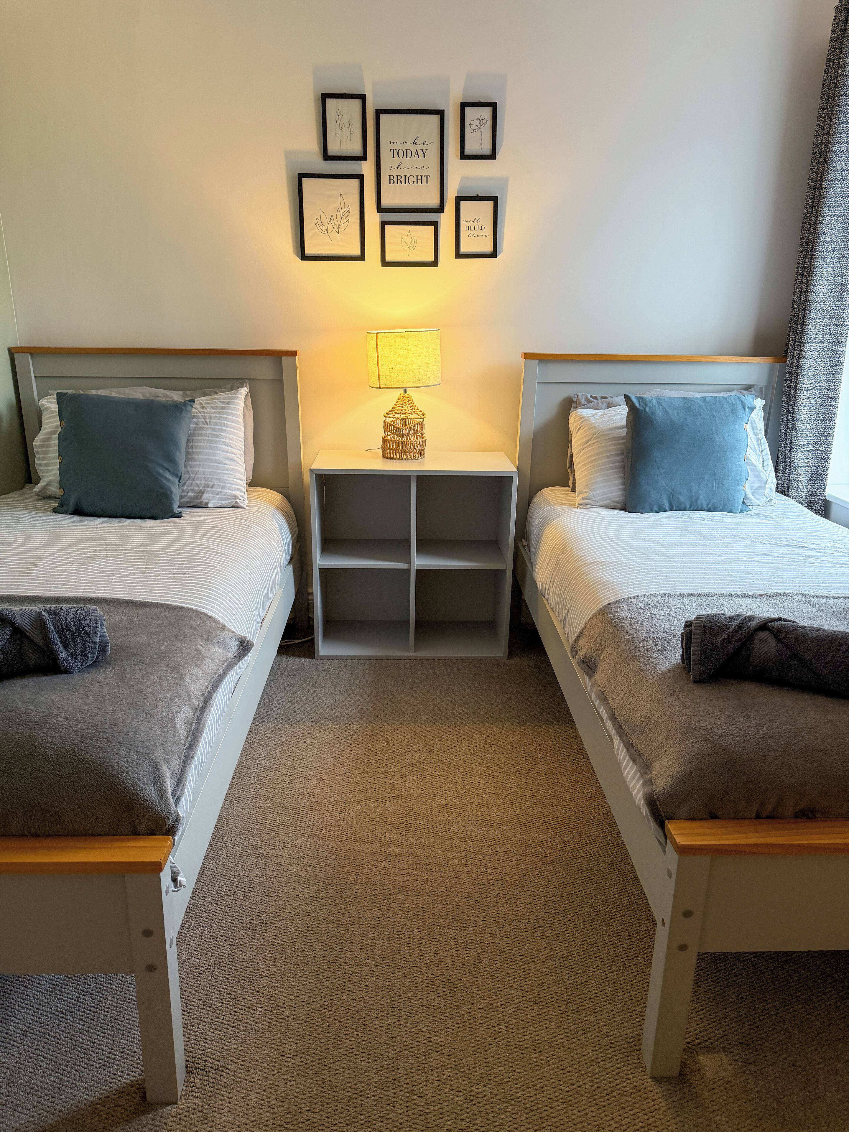 Une chambre d’hôtel avec deux lits, une table de chevet avec une lampe et un mur orné de citations inspirantes encadrées.