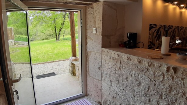 A room with a stone wall, a coffee machine, and a view of a grassy area through a sliding glass door.