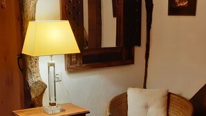 A cozy room with a wooden table, a lamp, a wicker chair, and a vase on a shelf.