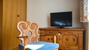 Una silla de madera con cojín, un televisor sobre un mueble de madera y un armario de madera en una habitación.