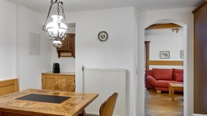 Un comedor con mesa y sillas de madera, una lámpara colgante, un radiador y un sofá rojo al fondo.