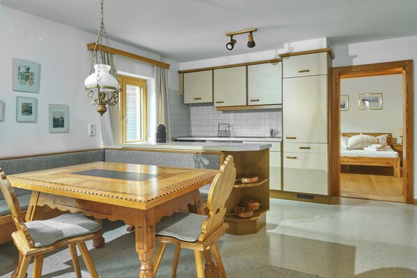 A kitchen with wooden cabinets, a dining table with chairs, and a small sleeping area with a bed.