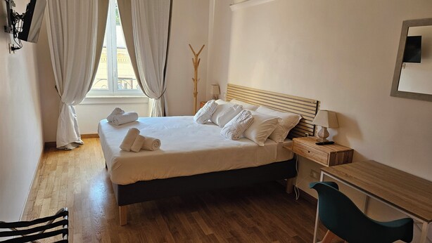 Une chambre d’hôtel avec un lit, un bureau, une chaise et une fenêtre avec des rideaux.