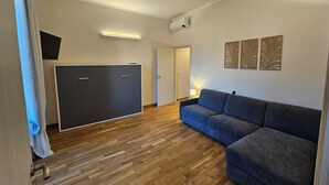 Un salon moderne avec un canapé d’angle, un téléviseur à écran plat, un climatiseur fixé au plafond et un plancher en bois.