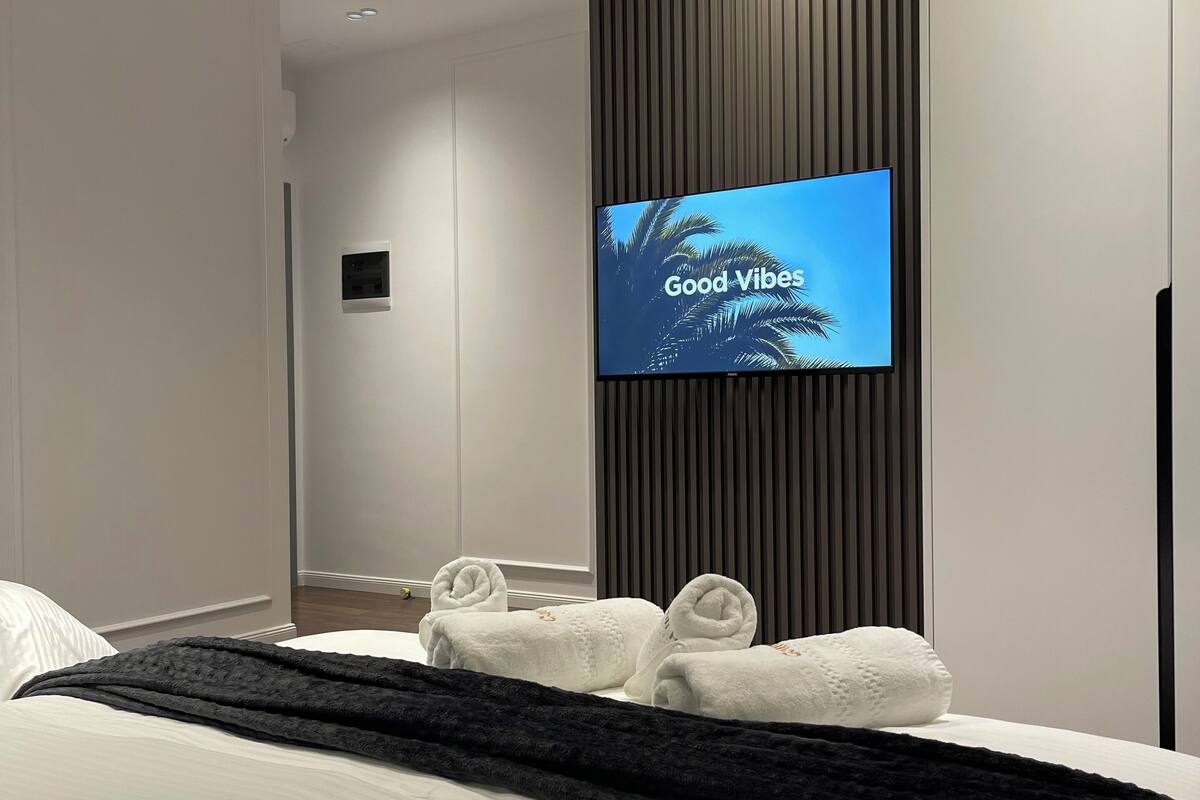 A modern hotel room with a large bed, a flat-screen TV mounted on a wall, and neatly folded towels.