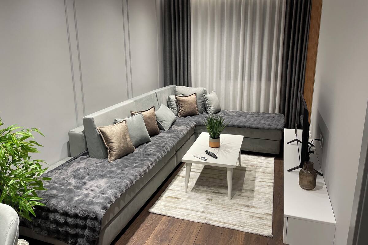 A modern living room with a grey sectional sofa, a small white coffee table, and a potted plant.
