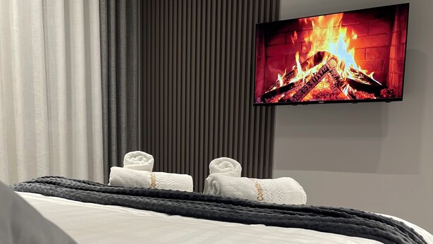 Una habitación de hotel con una cama, un televisor de pantalla plana mostrando una chimenea y una ventana con cortinas.