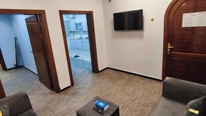 A hotel room with a flat-screen TV mounted on the wall, a wooden door with a notice, and a small ottoman with a remote control. - Al Rayhan Suites (Madinah)