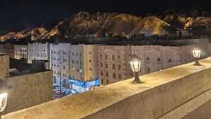 A nighttime view of a coastal city with illuminated buildings and a mountain backdrop. - Al Rayhan Suites (Madinah)