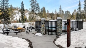 A stone fire pit with chairs, a stone wall, and a metal gate in a snowy outdoor area.