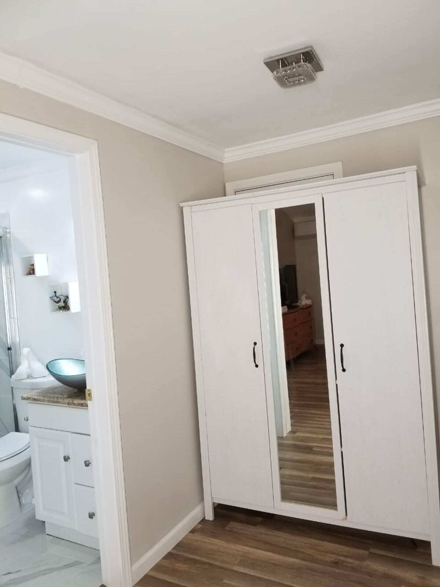 Ein Zimmer mit einem weißen Kleiderschrank, ein Badezimmer mit einem weißen Waschbecken und Spiegel sowie ein Holzboden.