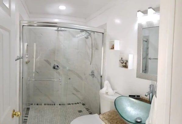 A modern bathroom with a glass-enclosed shower, a white toilet, a sink with a blue basin, and a mirror above the sink.