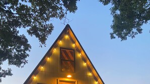 A wooden cabin with a balcony, a door, and string lights. - Tiny House at Wishing Creek (Henderson)