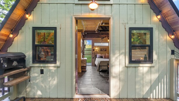 A cozy cabin with a wooden exterior, a porch with a patterned rug, and a grill outside. - Tiny House at Wishing Creek (Henderson)
