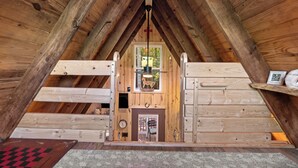 A wooden attic room with a sloped ceiling, a fireplace, a clock, and a small window with a view of trees. - Tiny House at Wishing Creek (Henderson)
