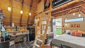 A rustic wooden interior with a kitchen, dining area, and a bedroom with a bed and window. - Tiny House at Wishing Creek (Henderson)