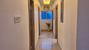 A hallway with a marble floor, wooden doors, and a ceiling light. - Hotel Yogita Inn  (Gaya)