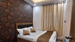 A bedroom with a bed, a ceiling fan, a door, and a window with curtains. - Hotel Yogita Inn  (Gaya)