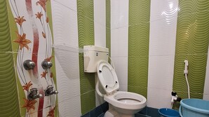 A bathroom with a toilet, a bidet, and a blue bucket. - Hotel Yogita Inn  (Gaya)