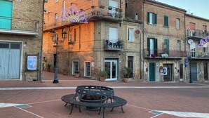A street with a round metal bench in the center, surrounded by brick buildings with balconies and potted plants.