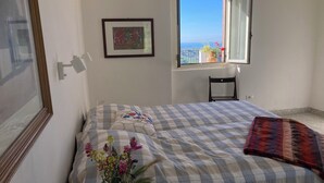 A bedroom with a bed, a window with a view, a chair, and a framed picture on the wall.