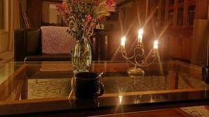A glass-top table with a vase of flowers, a candle holder with two lit candles, and a black mug.