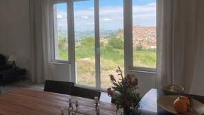 A dining area with a large window offering a view of a town and greenery.