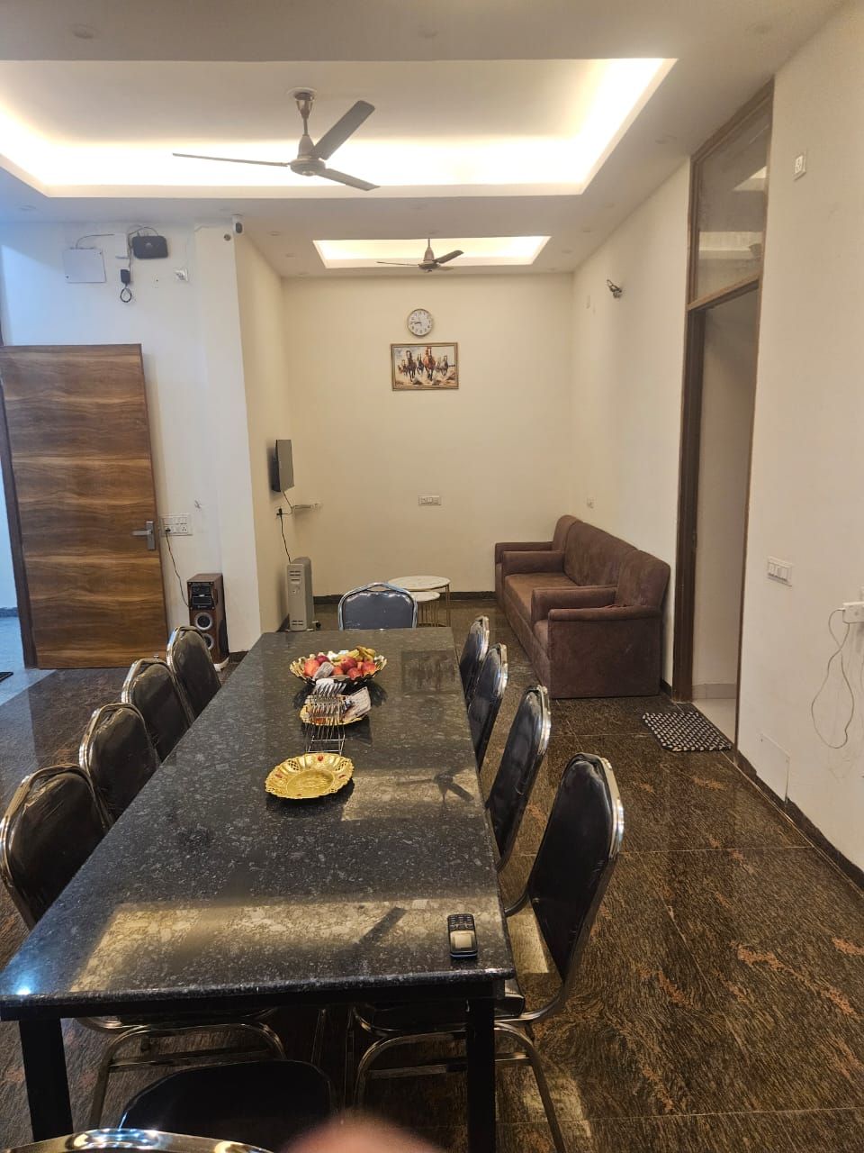 A conference room with a long table, chairs, a ceiling fan, a clock, and a framed picture on the wall.