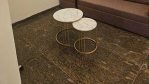 Een kamer met een bruine bank, twee kleine ronde tafels met gouden lijsten, een klok en een lijst aan de muur.