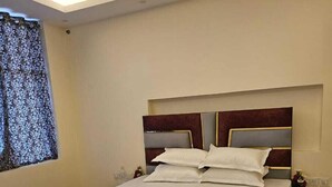 Een moderne slaapkamer met een groot bed, een hoofdbord met donkerhouten afwerking en een raam met een patroon gordijn.