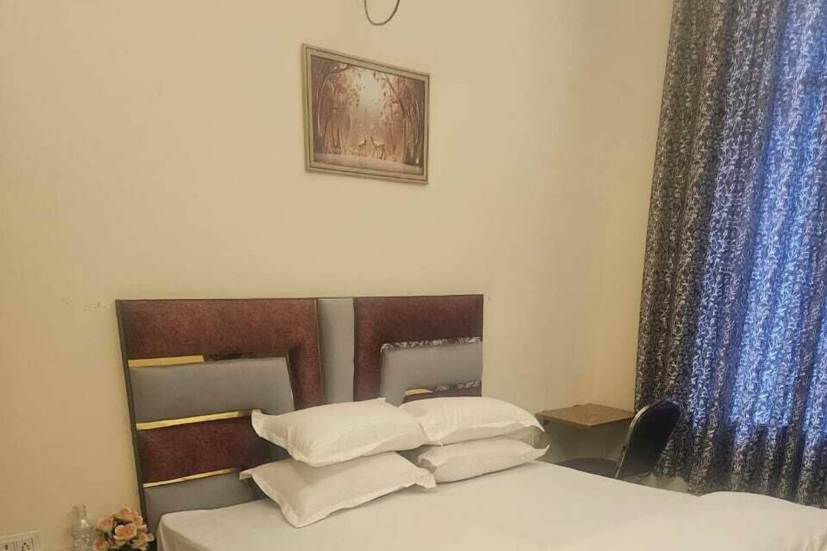 A neatly made bed with white linens, a dark headboard, and a small bedside table with a lamp and a vase of flowers.