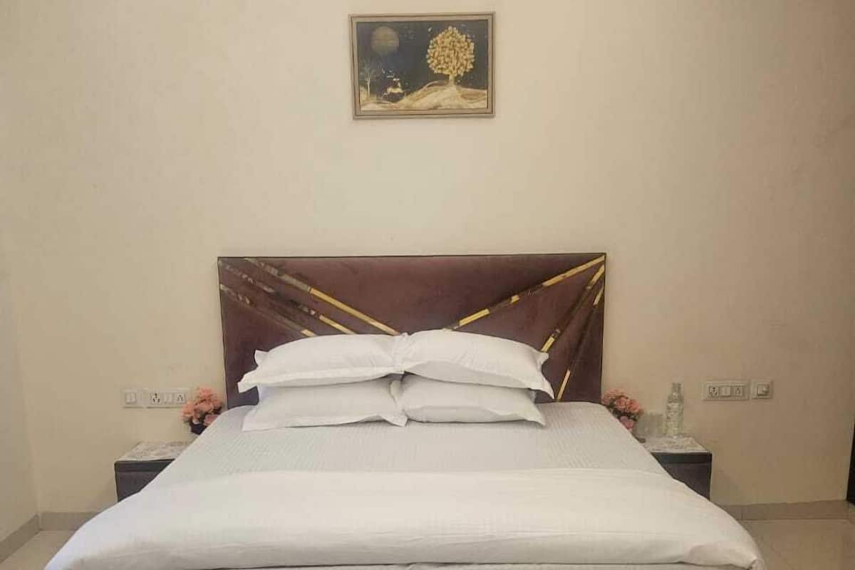A neatly made bed with a wooden headboard and white bedding, a small bedside table with a vase of flowers, and a framed picture on the wall.