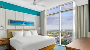 A hotel room with a large bed, a desk, a ceiling fan, a painting on the wall, and a large window offering a city view. - Luxury Wyndham Margaritaville suite with short walk to football game fullKitchen (Atlanta)