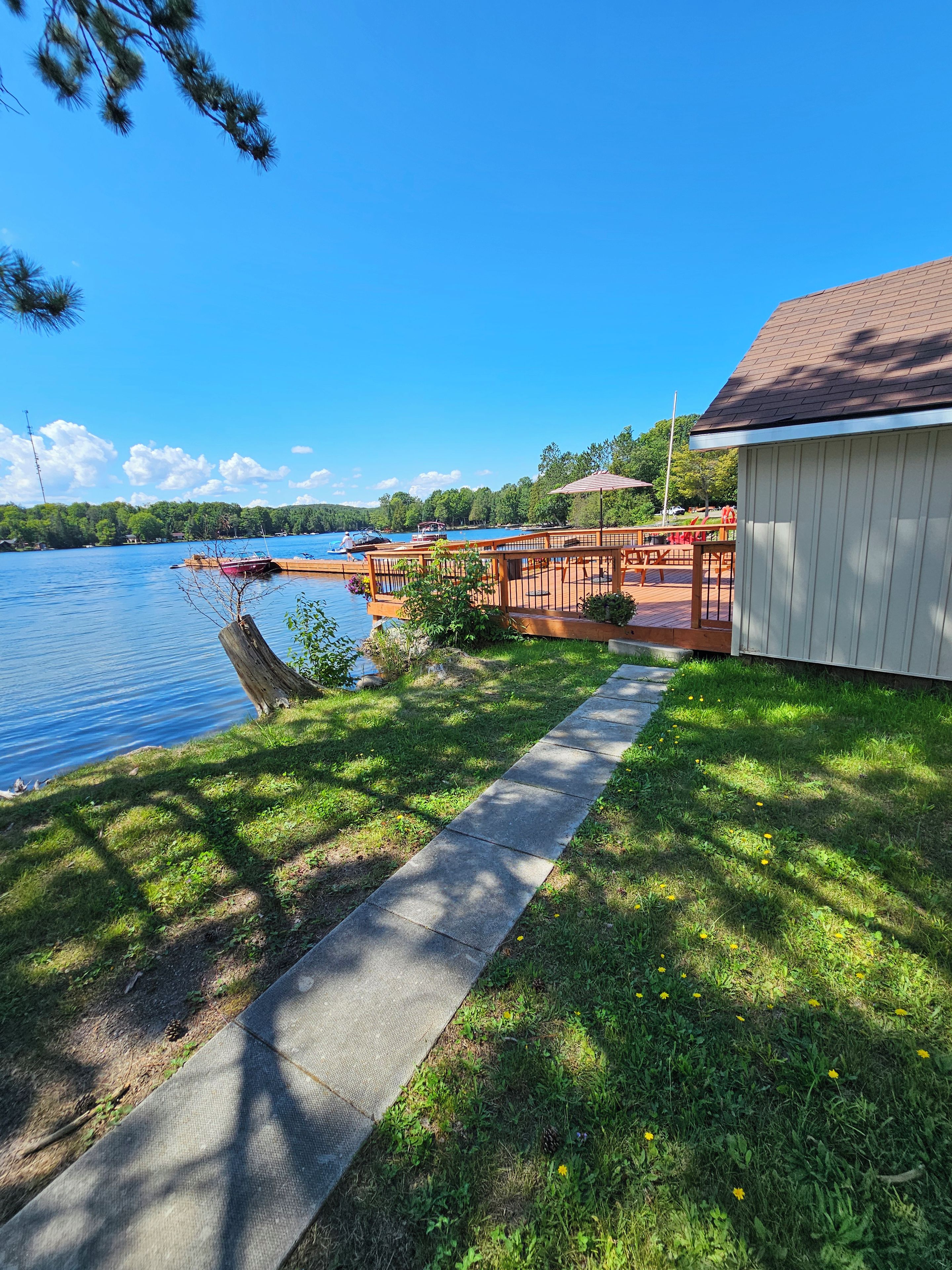 A lakeside property with a dock, a wooden deck, and a grassy area leading to a building.