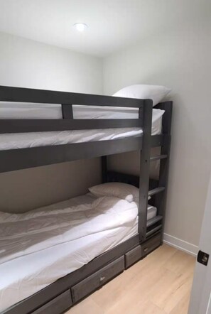 Ein Etagenbett mit zwei Schlafstellen, eine kleine Schublade unter dem unteren Bett und ein Lichtschalter an der Wand.