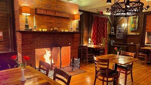 En mysig restaurang med en inbjudande inredning, en tegelbeklädd öppen spis, träbord och stolar.
