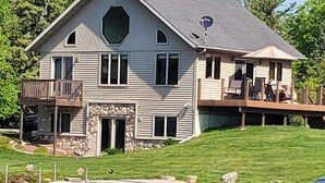 A two-story house with a stone foundation, a balcony, and a deck with outdoor furniture. - UP Lake Home with access to 3 lakes - fish, swim, relax! WIFI (Vulcan)