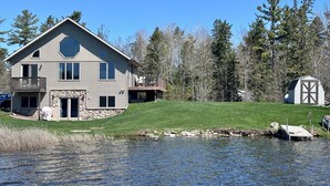 A two-story house with a stone foundation, a balcony, and a dock extending into a lake. - UP Lake Home with access to 3 lakes - fish, swim, relax! WIFI (Vulcan)
